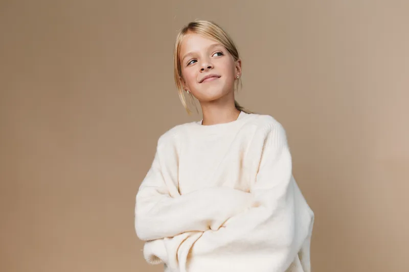 Authentic portrait of a young girl in a soft sweater, capturing a candid moment of playful innocence and school life in a warm lifestyle setting.