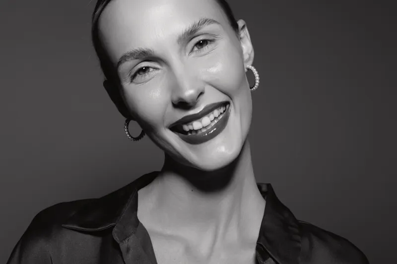Close-up of a smiling Caucasian woman with light skin and earrings in black silk shirt. Studio portrait with soft lighting and joyful emotion. Concept of happiness and beauty.