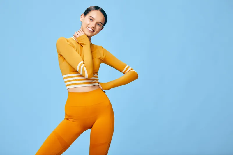 Fitness and sport themed portrait of a woman in bright orange activewear posing confidently against a blue studio backdrop, highlighting flexibility, strength and vibrant athletic style.