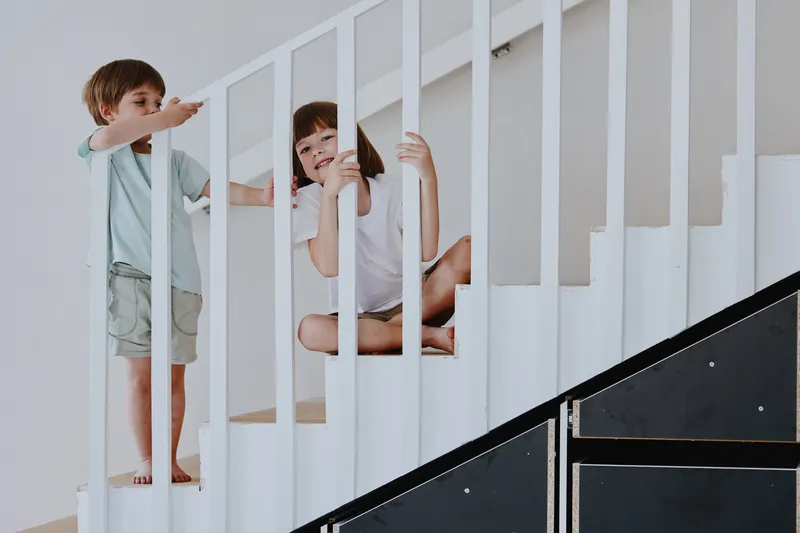 Happy children enjoying time on a staircase, playfully interacting and smiling, showcasing joy and innocence in a bright and modern environment.