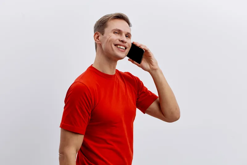 smiling man talking phone wearing red t-shirt looking away isolated on gray background concept video call different time zones communication technology