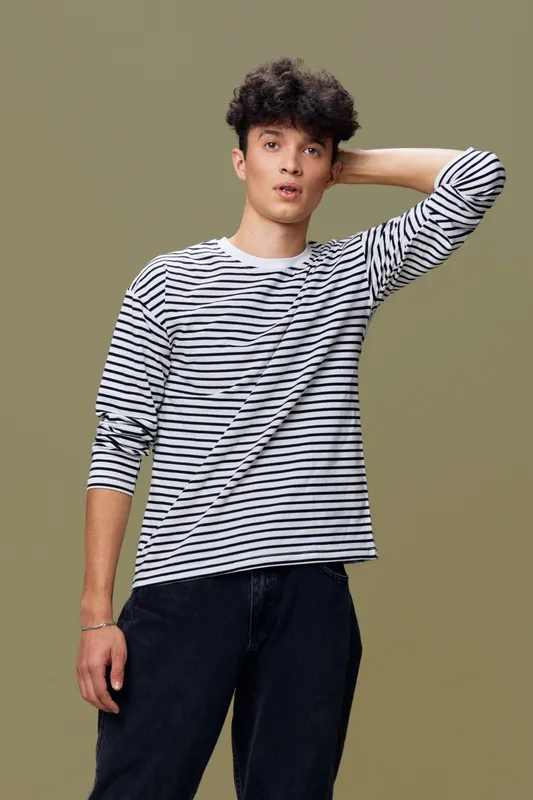 young man wearing striped long sleeve shirt posing with hand behind head against plain olive background in casual style