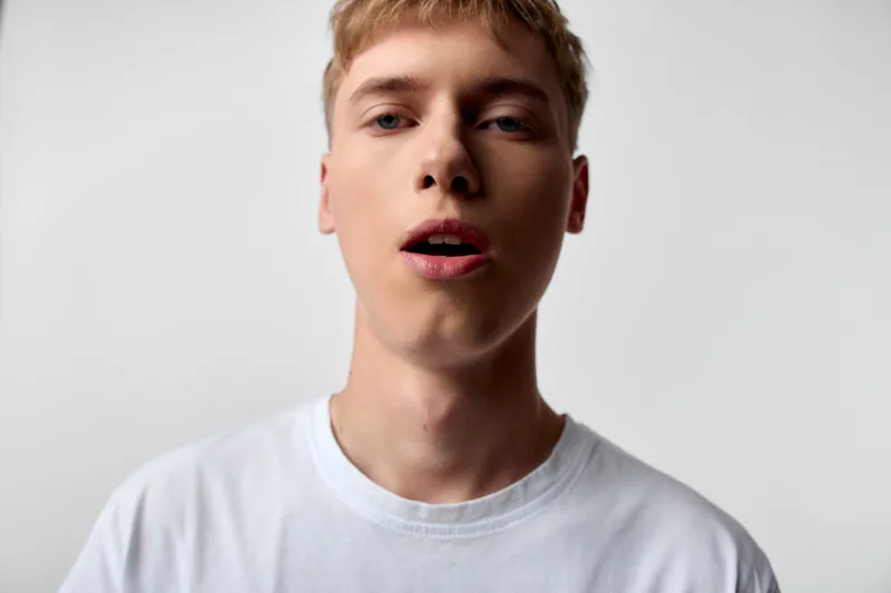 Young man, mouth, speaking, studio, expression, white shirt, close up, face, talking, vocal, lighting, neutral background, casual fashion, headshot style, facial energy, candid moment, everyday