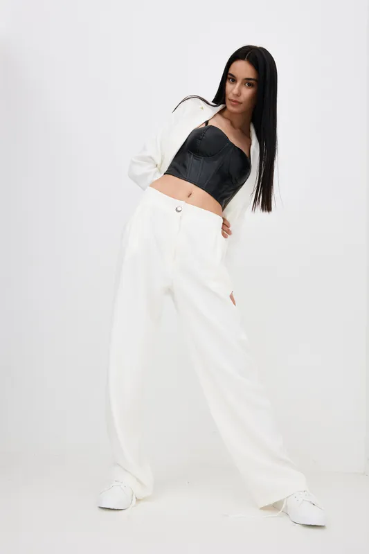 stylish woman posing confidently in white pants and black corset against white background, with straight long hair and casual shoes, minimalistic studio look
