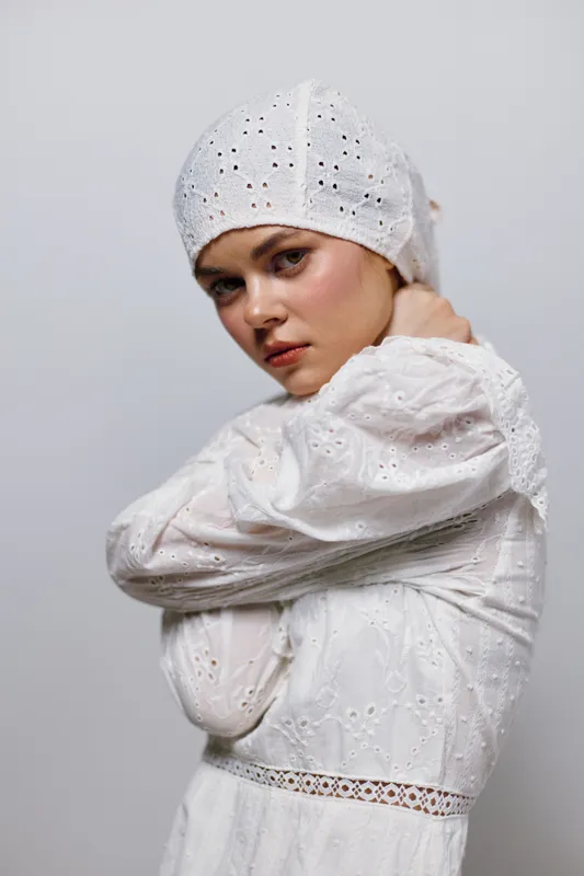 Young woman in a white dress with a headscarf, showcasing serene emotions against a neutral background, ideal for health and beauty concepts
