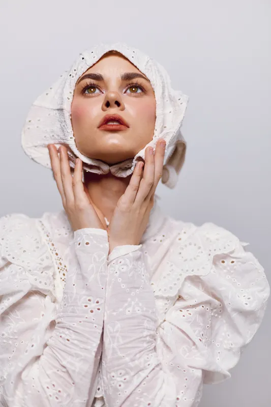 Elegant portrait of a young woman in a vintage white dress, showcasing emotions of hope and contemplation against a soft neutral background