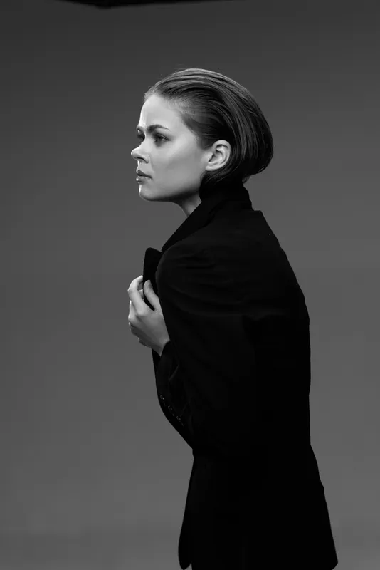 Black and white profile of a serious woman with braided hair wearing a dark jacket against a plain background.