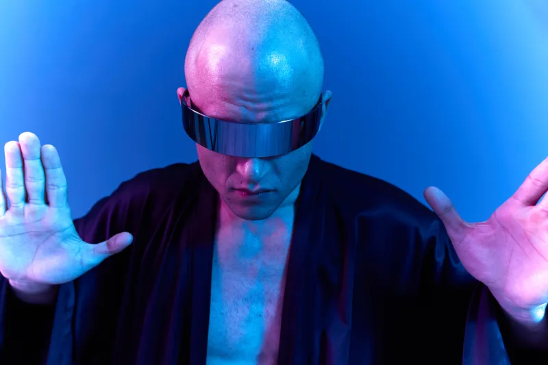 Futuristic man with sleek sunglasses and a dramatic pose, surrounded by vibrant blue and violet lighting. The image captures a unique, modern aesthetic.