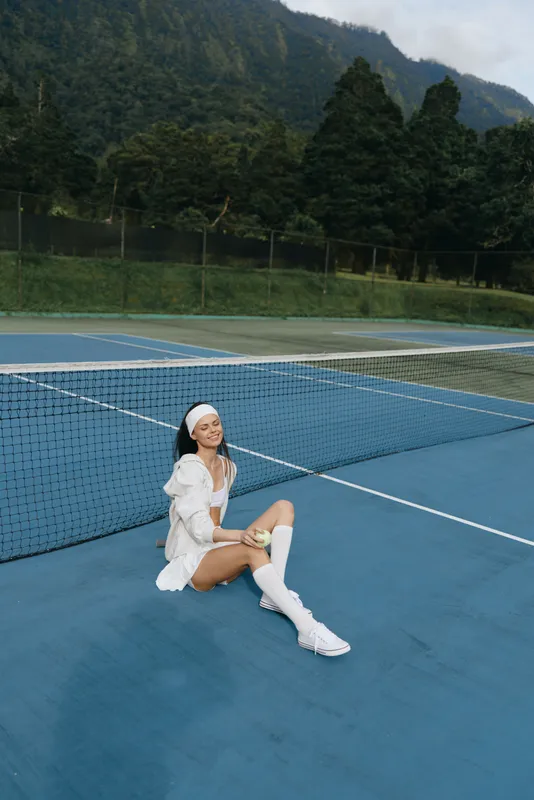 Young woman enjoying a game of tennis on a blue court, wearing sporty attire, conveying joy and energy amidst a scenic background with lush greenery