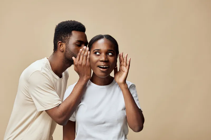 Young black couple sharing a secret, vibrant emotions, neutral background, intimate moment, playful interactions, communication concept