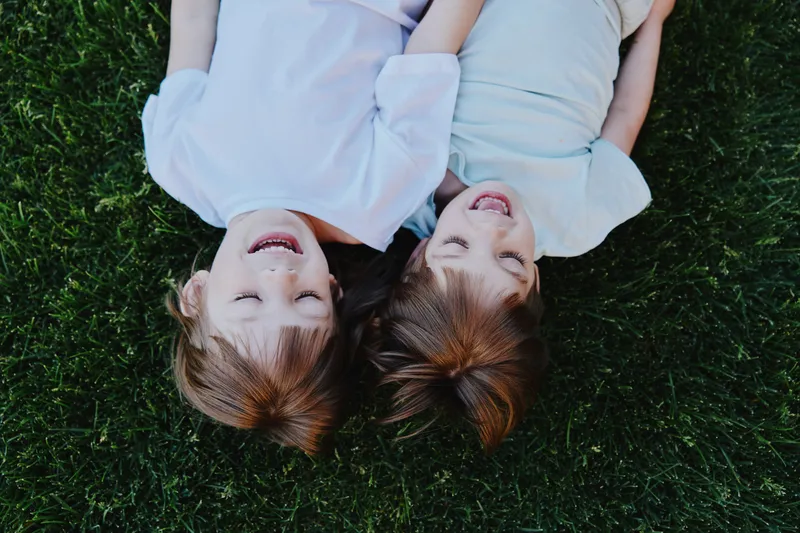 Joyful children laughing together on green grass, showcasing happiness and carefree childhood moments in a sunny outdoor setting.