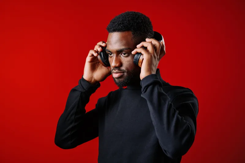 Young Black man wearing headphones against a vibrant red background, focused and enjoying music, capturing emotions of relaxation and engagement