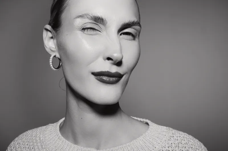 Close-up portrait of a fair skinned Caucasian woman winking with red lips in monochrome. Concept for beauty, confidence, emotion, and facial expression in studio lighting.
