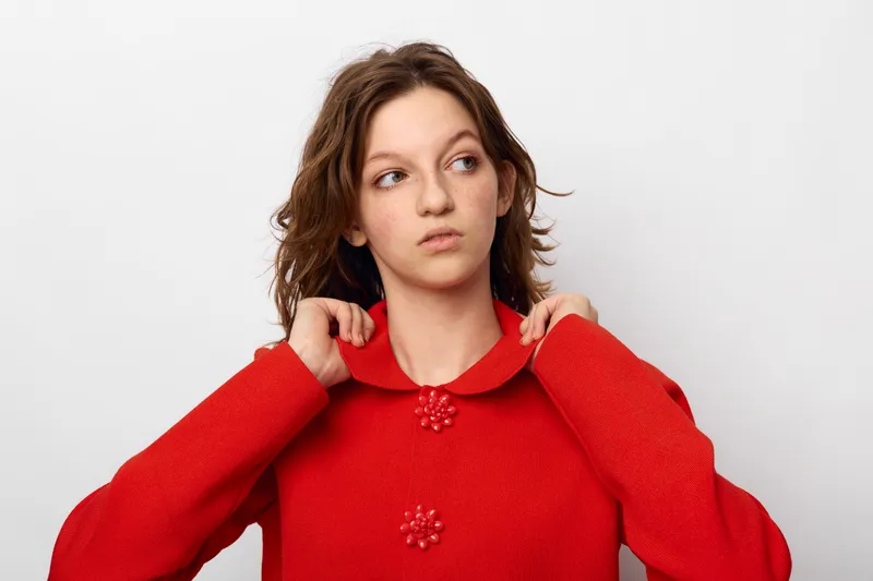 Young woman in red sweater looks to the side with thoughtful expression on white background. Casual style, portrait, fashion, and natural light concept.
