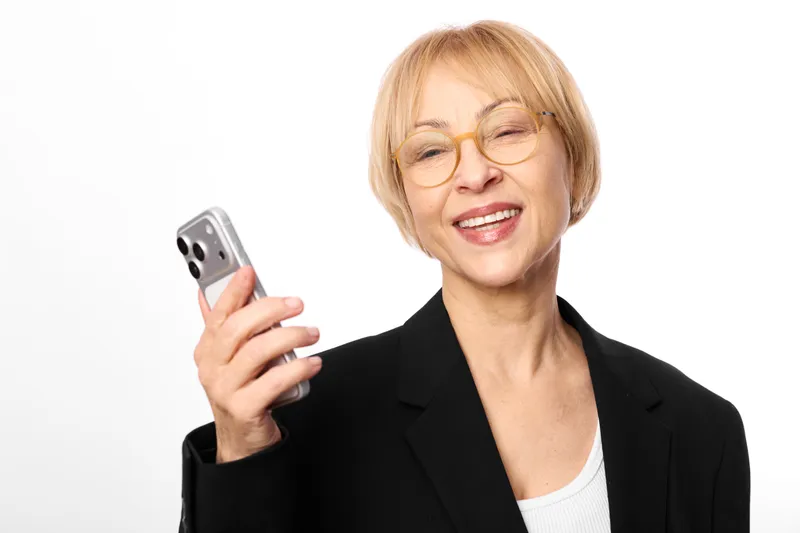 Senior woman with glasses smiling, holding smartphone in business portrait isolated on white background, modern communication with friendly expression today