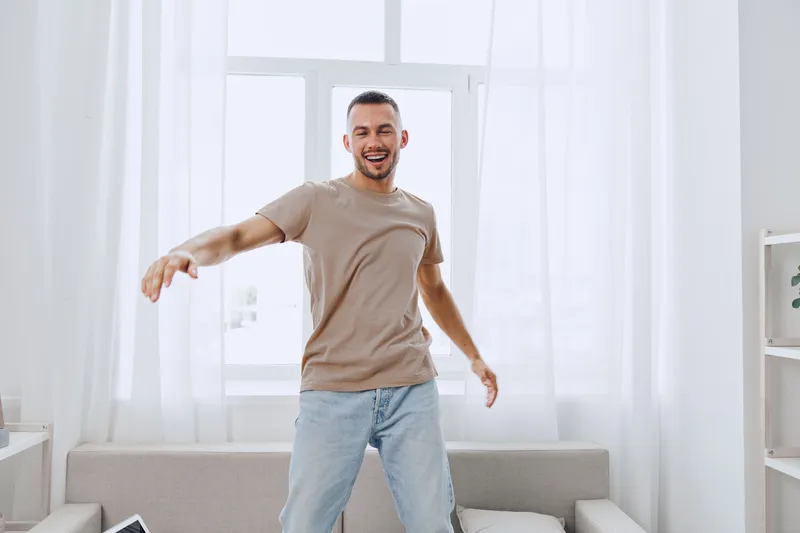 Happy man dancing joyfully in a bright living room, wearing a casual outfit. The energetic vibe captures the essence of contemporary home life and wellbeing.
