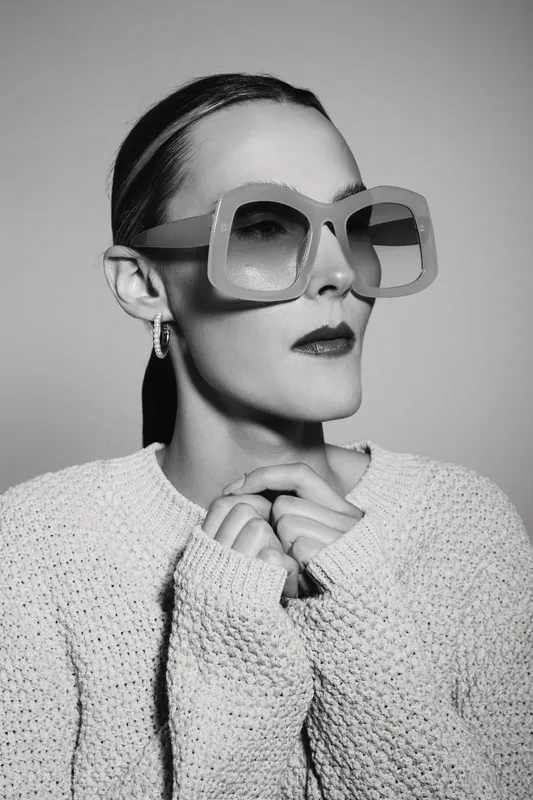 White woman with fair skin wearing large sunglasses and a knitted sweater poses in a black and white studio portrait. Concept of fashion and style.