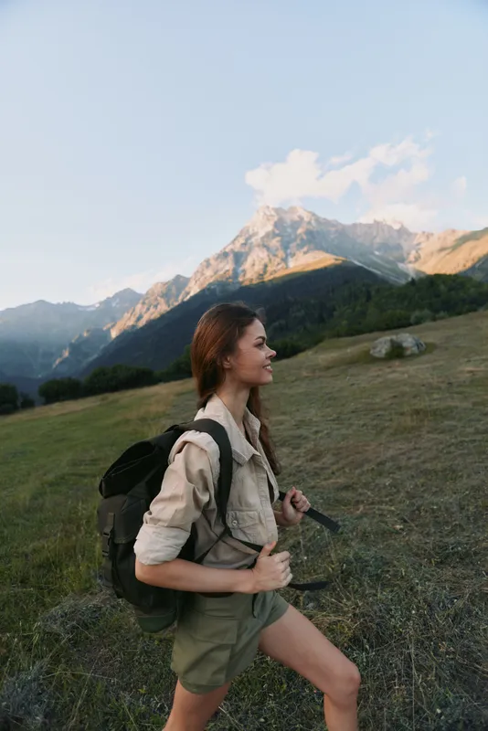A woman hiker climbs a grassy hillside under a clear sky, with a backpack, embodying an active outdoors lifestyle and mountain exploration.