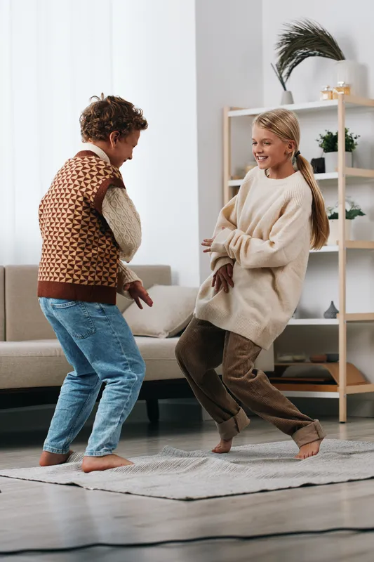 Authentic moment of two kids dancing in a bright living room, a playful game creating laughter, casual outfits, warm light, and a genuine lifestyle scene.