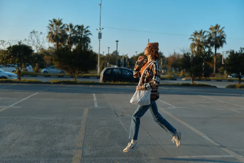 Woman jump in parking lot eating icecream in casual outfit, candid lifestyle shot with authenticity and golden hour glow, mindful living and emotional storytelling in urban sunset scene.