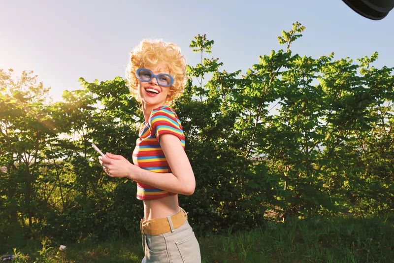 Woman lifestyle retro outdoors sunlight smile sunglasses striped top blonde, joyful moment captured in warm vintage color, candid outdoor portrait with carefree mood
