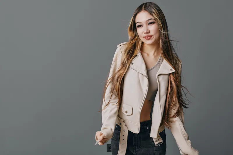 Young woman posing in beige jacket and crop top with long hair against gray background, casual fashion style and relaxed confident expression in studio.