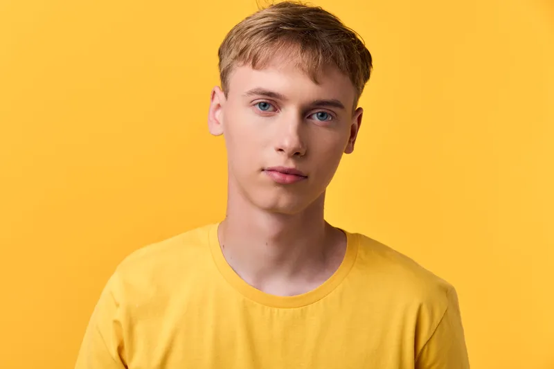 Young man, yellow shirt, yellow background, front view, studio shot, casual attire, facial expression, clean minimal lighting, showcasing a bright color palette and approachable fashion mood