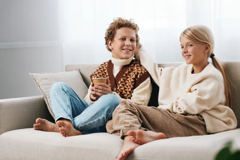 Authenticity shines as siblings enjoy a playful moment on a cozy sofa, highlighting a school age lifestyle and a casual game in a warm home setting.