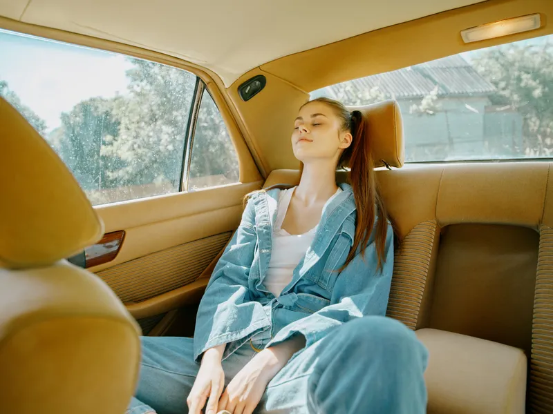 Young woman resting peacefully in a car, wearing casual denim outfit, exuding calmness and relaxation, with a sunny background and warm color palette.