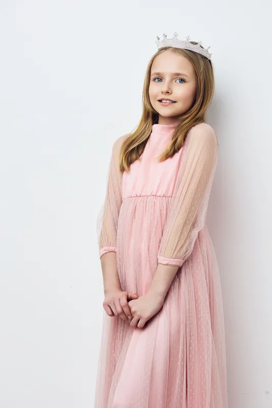 A young girl in a pink dress and a crown, smiling against a light background, embodying innocence and joy, perfect for children s photography, birthday themes, and royalty concepts