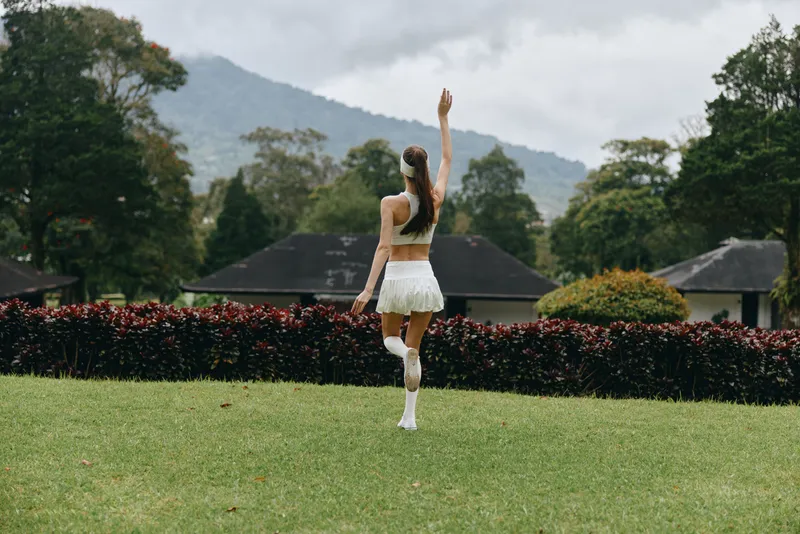 Young woman wearing a white skirt and top dancing joyfully in a lush green park, showcasing a carefree spirit against a natural backdrop