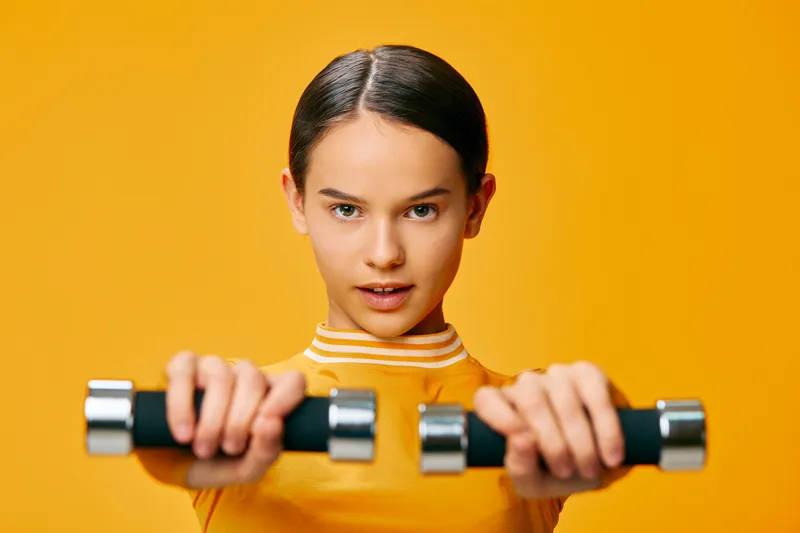 Fitness woman in a bright orange studio holding dumbbells for a workout and training session. Focused athlete, sport motivation, health and strength.