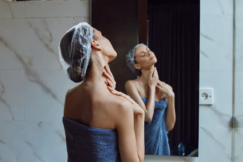woman with towel applying skincare in bathroom mirror, morning routine, fresh skin care, serene self-care moment, natural beauty, wellness focus