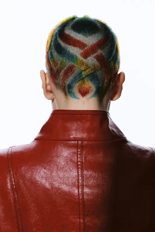 Woman with colorful geometric hair tattoo wearing a red leather jacket, vivid hairstyle pattern, creative and modern fashion statement in studio light.