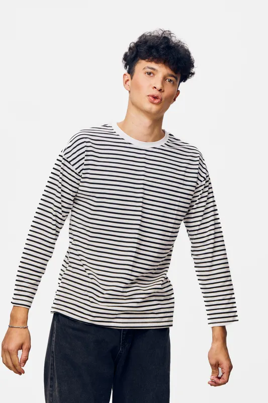 young man wearing striped long sleeve shirt standing against white background with expressive face and casual pose, modern fashion style