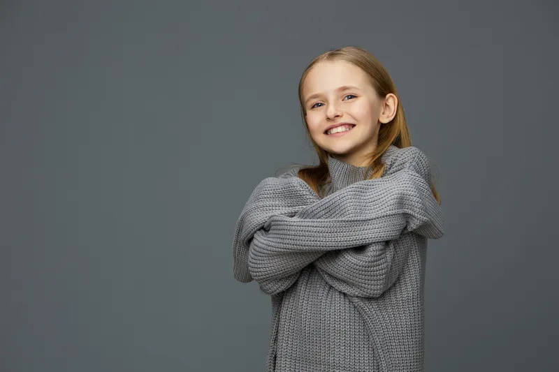 Smiling girl in a cozy gray sweater against a minimalistic background, expressing happiness and comfort Perfect for lifestyle and children s themes