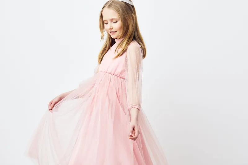Cheerful young girl in a pink tulle dress, elegantly twirling, showcasing joy and innocence against a clean, neutral background, perfect for fashion and children s wear concepts