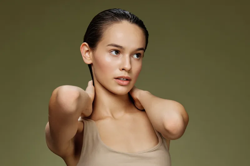 Young woman with smooth skin and wet hair poses against a soft green background, showcasing natural beauty and minimalistic style
