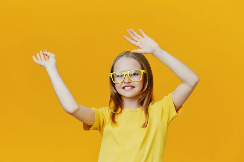 Happy girl in yellow t shirt and glasses celebrating on vibrant yellow background, showcasing joy and positivity