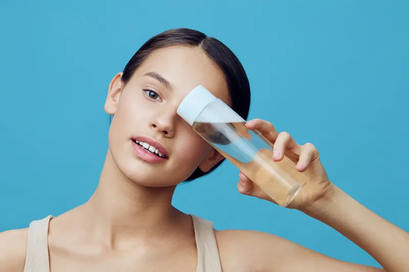 Young woman showcasing skincare product, radiating confidence with a blue background, emphasizing beauty and self care, ideal for wellness and skincare themes