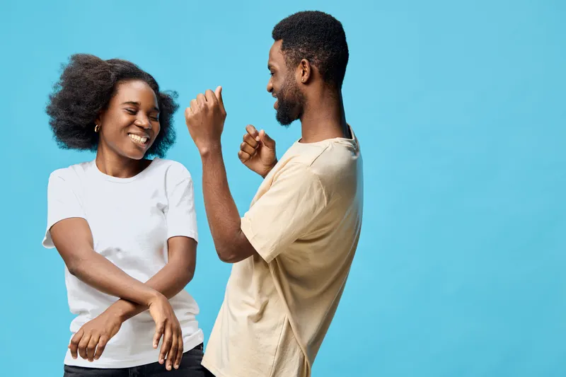 Joyful diverse couple dancing together against a bright blue background, showcasing happiness and connection in casual outfits