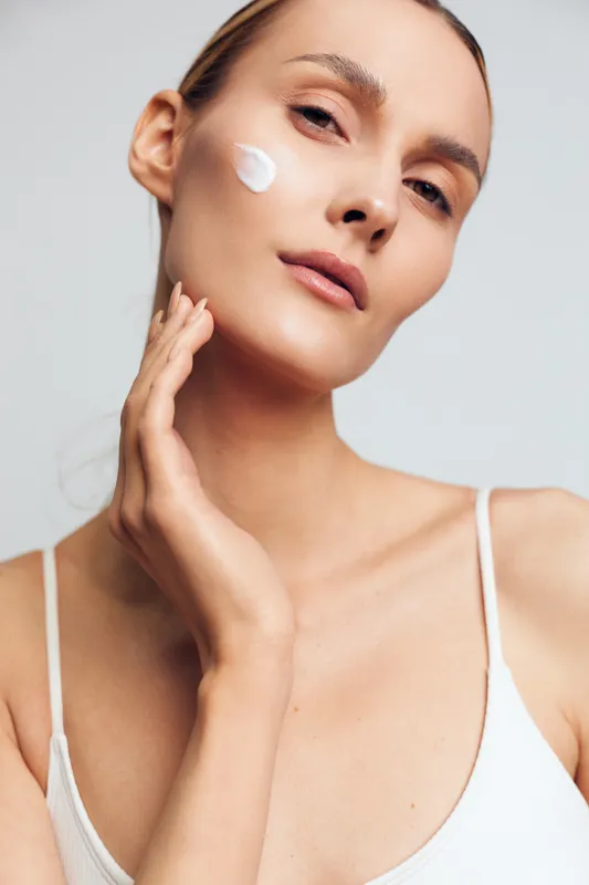 Woman skincare face cream beauty spa treatment portrait, young adult applying moisturizer on smooth skin, calm relaxed mood, isolated on light background
