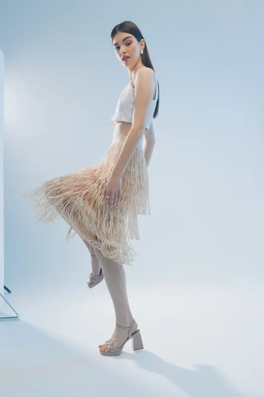 Young woman in stylish fashion outfit poses in studio with light background. Her beauty and elegance are highlighted by the flowing skirt and confident expression. Concept of woman beauty fashion.