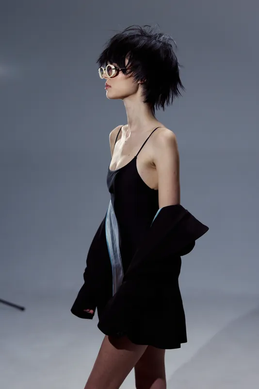 stylish woman wearing black dress and sunglasses walking with confident posture indoors
