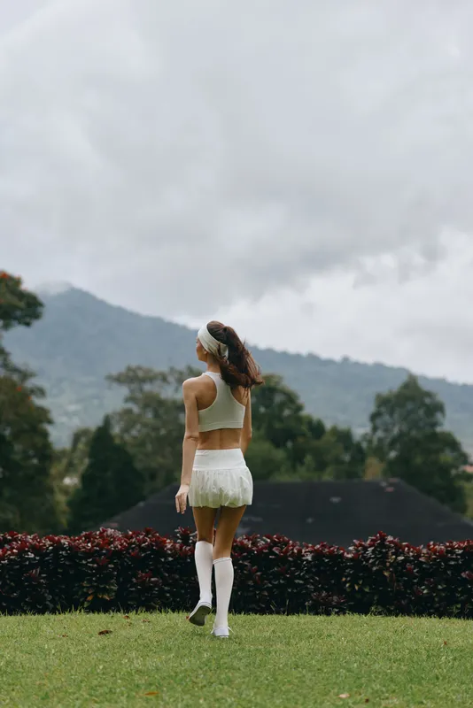 Young woman in a white sports outfit walking in nature, showcasing a healthy lifestyle and confidence, with mountains in the background and a fresh color palette