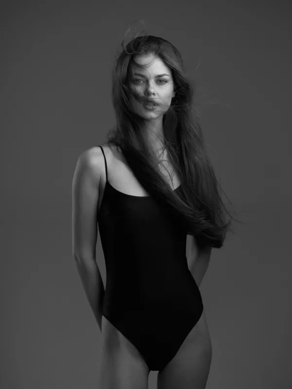 Black and white portrait of a woman in a black swimsuit with flowing hair, posing against a plain background with a calm expression.