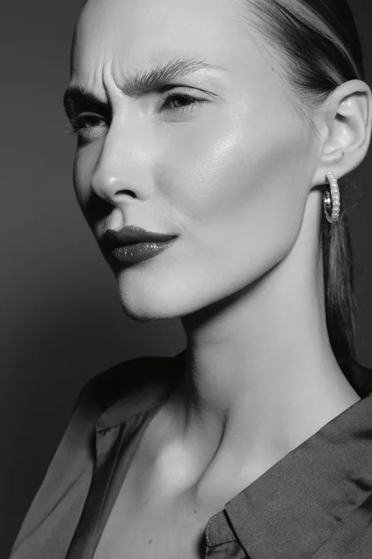 Close-up of a serious young white woman with light skin and slicked hair looking sideways in black and white portrait studio lighting.