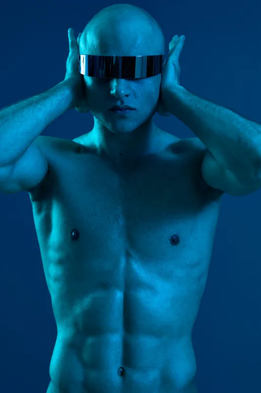 Stylish man wearing futuristic sunglasses, posed against a vibrant blue background, creates a striking and modern black and white effect.