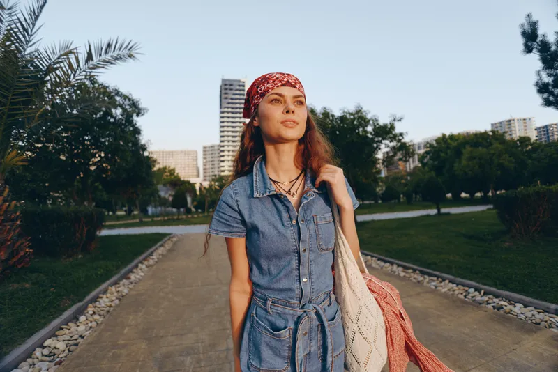 Lifestyle woman in modern boho-western denim street style walking outdoors at golden hour with film color effect and red bandana, urban background and casual confidence.