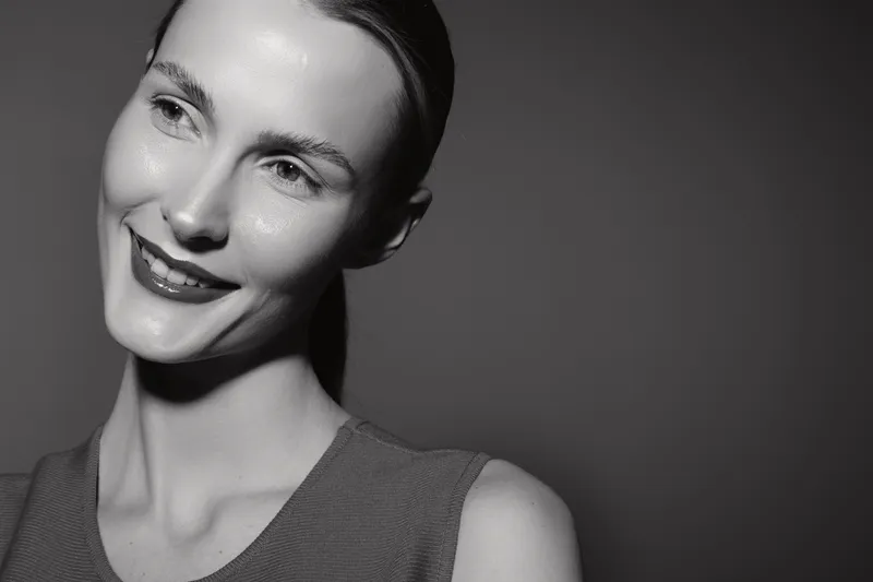Portrait of a smiling Caucasian woman with light skin looking away, wearing a sleeveless top. Studio lighting highlights natural beauty and positive mood in black and white.